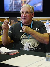 Photo d'un homme d'un certain âge, portant des lunettes et tenant un stylo.