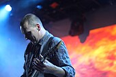 Justin Broadrick playing guitar over a backdrop of fire