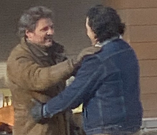 Two men with dark hair, both wearing thick jackets, embracing each other