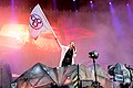 Photo en couleur d'une femme chantant sur une scène, elle tient dans sa main un drapeau