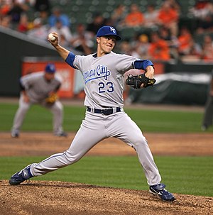 A young man in a blue cap and gray baseball uniform with blue lettering on the chest, including the number 23, pitches a baseball right-handed.