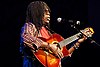 alt=A man with hair braids is wearing sunglasses and playing a guitar. Milton Nascimento