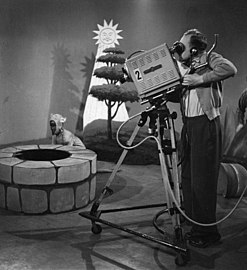 Cadreur de télévision utilisant un trépied en bois sur un Y en tubes légers sur roulettes (années 1950).