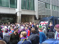 A crowd of people and a police van outside a building.
