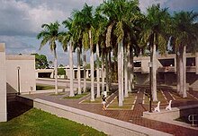 The New College of Florida campus. In front of a dormitory building to the right is a grid of palm trees arranged in a tiled courtyard.