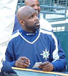 A man in a navy blue warmup jersey signs an autograph while looking up.