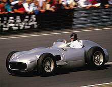 Photo of Juan Manuel Fangio driving a silver Mercedes on a race track