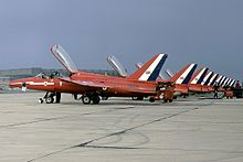A squadron of one-man jet aircraft, with their canopies open, lined up at a military airbase.
