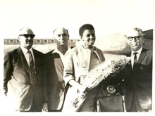 Makeba standing before an aeroplane flanked by three men