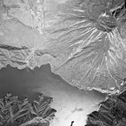 Photo noir et blanc d'un lac au pied d'un volcan, vu du ciel.