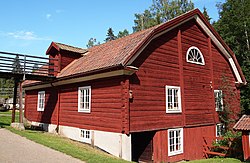 Rödmålad byggnad med vita fönsterfoder, fotad så att man ser en långsida och en kortsida.