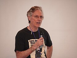 Charles Pellegrino wearing a black print t-shirt, speaking into a microphone