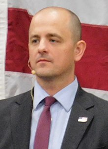 McMullin, wearing a microphone, in front of the red and white stripes of a U.S. flag