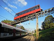 A TiLo FLIRT train in the station, and a car of the funicular passing overhead.