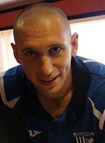 A young man with a shaven head, wearing a blue and white T-shirt