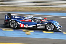 Photographie dune voiture de sport-prototype bleue, rouge, blanche et noire, de profil, sur une piste.