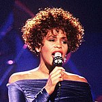 An African American woman with curly hair sings into a microphone