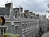 A grey and white row of houses with a complex roofline and a taller projecting section at the end, seen from just below roof level.