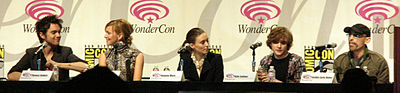 Five actors sitting at a table in front of individual microphones