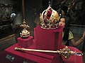 Dans un écrin rouge en vitrine figurent un sceptre richement décoré de joyaux dont le manche est blanc et semble clairement fait d'ivoire, ainsi qu'une couronne d'or décorée elle aussi de joyaux, de perles, et d'autres parties en ivoire.