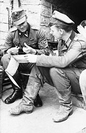 Two soldiers in different uniforms sitting and looking over a map