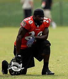 Ed Reed in a Baltimore Ravens jersey resting on one knee with his helmet on the ground in his hand.