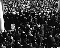 The inauguration of John F. Kennedy in 1961, as seen from behind. Most men have their hats off; however a few top hats can be distinguished, some by the shininess of the hat's flat crown