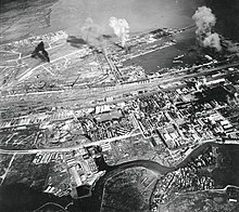 Black and white aerial photograph of a city and port area with explosions taking place