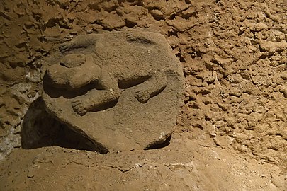 Pierre sculptée beige posée sur un tas de terre posée sur un mur de terre.