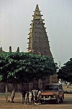 A mosque with a minaret in Sudano-Sahelian style, an old car and people in front