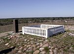 A black stone pillar and a white fence marking the site.