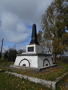 Photographie d'un obélisque dans un cimetière avec une plaque commémorative.