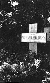 Black-and-white photograph of a wooden cross on a grave, bearing the inscription "Oberst Werner Mölders, 18. 3. 1913 – 22. 11. 1944."