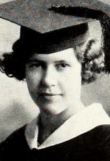 A smiling young white woman with curly hair, wearing a mortarboard cap