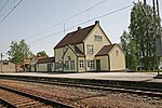 Foto eines Bahnhofsgebäudes mit Gleisen im Vordergrund