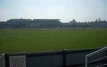 Green pitch with a building in the background.