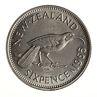 A silver-colored New Zealand sixpence, 1965, featuring a Huia bird on a twig.
