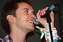 A young man in a checkered shirt sings into a microphone.