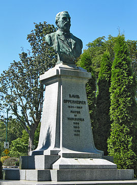 A bronze bust sits on a pillar in a city park.