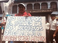 Guatemalan man in front of Constitutional Court holding sign that says "no queremos el saque do los recursos de Guatemala fuera toda minera"