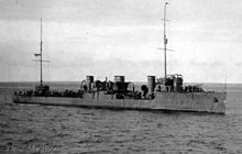 The black-and-white photograph depicts a period when the warship was sailing on the open sea. The ship is captured from an oblique angle with its bow pointed towards the right. The sea is calm, with light waves, and the sky is clear without any clouds. The ship is flying the flag of Estonia, although the Russian-language caption on the photograph mentions its Russian name, Miklucha Maklai.