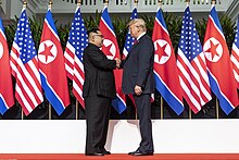 Trump and Kim shake hands on a stage with U.S. and North Korean flags in the background