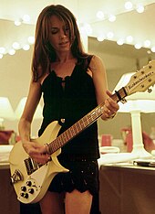 A woman playing a light-colored electric guitar