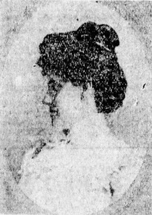 A woman with dark hair (pinned and styled on top of her head) looks to her right.