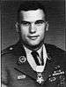 Head and shoulders of a white man with short dark hair wearing a military jacket with a star-shaped medal hanging loosely from a ribbon around his neck.