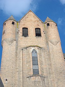 Photo couleur d'une construction en briques rouges. Le haut bâtiment présente une longue et fine ouverture à arc trifolié en pierre à son sommet. Le fronton de la toiture est encadré de deux échauguettes.