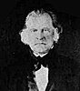 A man with bushy, white hair wearing a black jacket and bowtie and white shirt