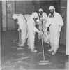 Five members of a clean-up crew scrub the floor while wearing full protective radiation suits.