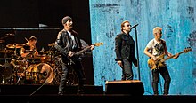 A color photograph of members of the band U2 performing on stage