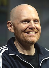 A bald man with red and gray facial hair smiles and looks off-camera.